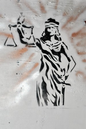 A spraypainted stencil of Lady Justice holding her sword in one hand, her scales aloft in another.